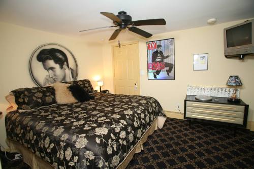 A cozy bedroom featuring a large bed with floral bedding, Elvis posters, a ceiling fan, and a TV on the wall.