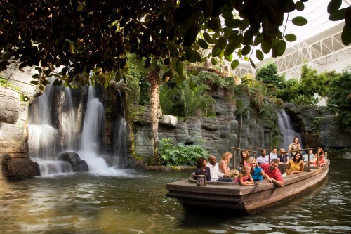 A group of people enjoying a boat ride near a lush waterfall and greenery in a tropical setting.