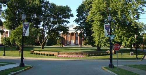 A view of a college campus with a large building, trees, and street signs, creating a welcoming academic atmosphere.