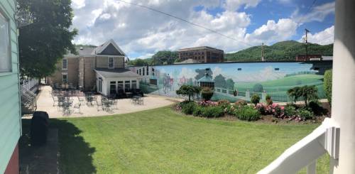 A vibrant mural on a building, surrounded by a grassy area with flowers and outdoor seating under a blue sky.