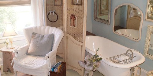 A cozy bathroom with a vintage bathtub, a white armchair, and decorative mirrors on the walls.
