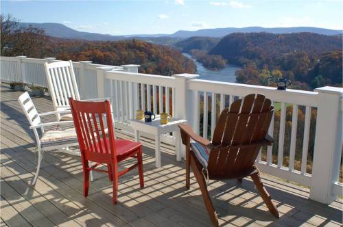 A scenic view from a deck with chairs overlooking a river and autumn-colored mountains in the background.
