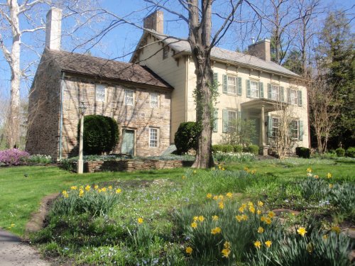 A historic house with stone and wooden architecture, surrounded by blooming flowers and lush greenery.