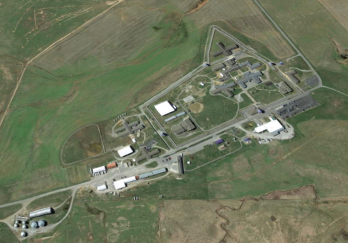 Aerial view of a large facility surrounded by green fields, featuring multiple buildings and roads.