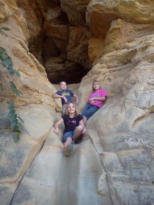 Three people sitting on a rocky slope inside a cave, surrounded by natural stone formations.