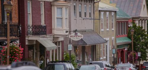 Charming street view of a small town with shops, a bistro, and parked cars under a cloudy sky.