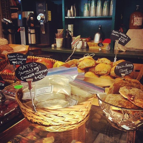 A cozy bakery display with muffins, scones, and baked goods in baskets, featuring handwritten price tags.