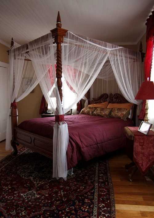 A cozy bedroom featuring a four-poster bed with sheer drapes, rich bedding, and warm wooden accents.