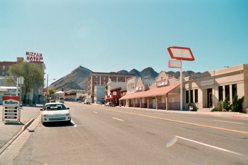 A quiet street scene featuring the Mizpam Motel, mountains in the background, and a parked car under clear blue skies.
