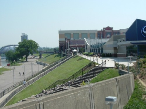 A view of a riverside promenade with grassy slopes, buildings, and a staircase leading down to the water.