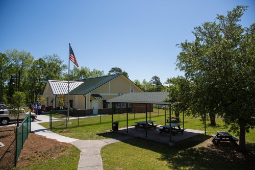 A yellow building with a green roof, picnic areas, and an American flag, surrounded by trees and clear blue skies.