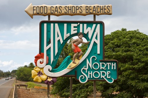 Colorful sign for Haleiwa, North Shore, featuring a surfer and flowers, with directions to food, gas, shops, and beaches.