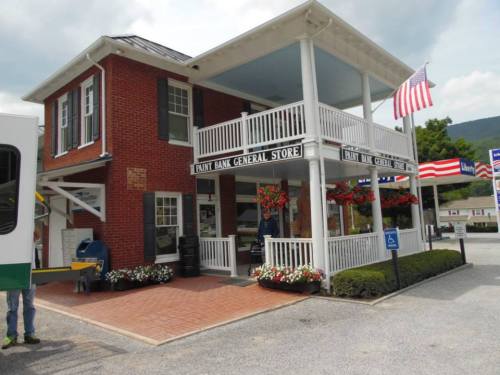 A brick building with a porch, labeled "Paint Bank General Store," featuring flower boxes and American flags.