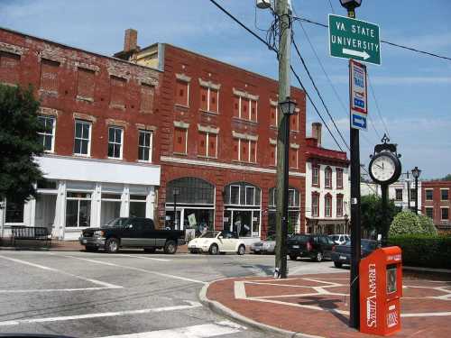 A street view featuring brick buildings, a clock, and a sign for Virginia State University. Cars are parked nearby.