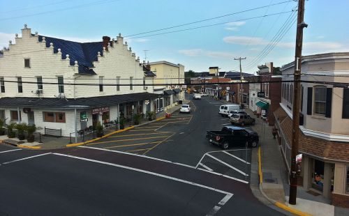 A view of a small town street with shops, parked cars, and a clear blue sky.