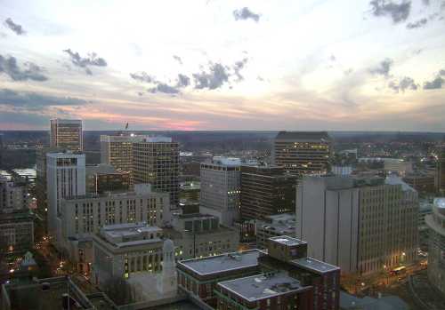 City skyline at dusk with buildings illuminated and a colorful sky filled with clouds.