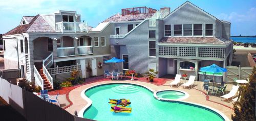Aerial view of a house with a pool, surrounded by lounge chairs and umbrellas, in a sunny outdoor setting.