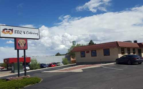 A BBQ restaurant with a sign, featuring a lion logo, surrounded by cars and under a cloudy sky.