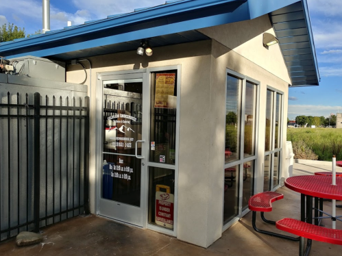 A small building with large windows, a blue roof, and red picnic tables outside, surrounded by a fence.