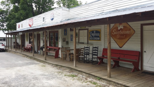 A rustic storefront with wooden benches, signs for ice cream and bread, and a gravel path in front.