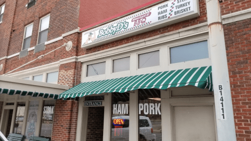 Exterior of Bobby D's BBQ restaurant, featuring a green and white striped awning and a sign listing menu items.
