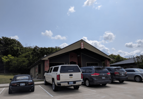 A BBQ restaurant with a parking lot filled with cars under a partly cloudy sky.