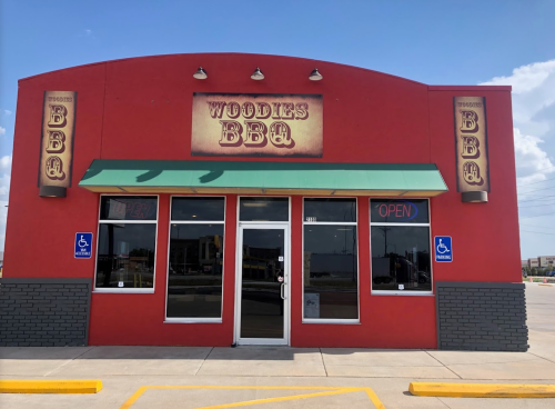 Exterior of Woodies BBQ restaurant, featuring a red facade, green awning, and "OPEN" sign in the window.