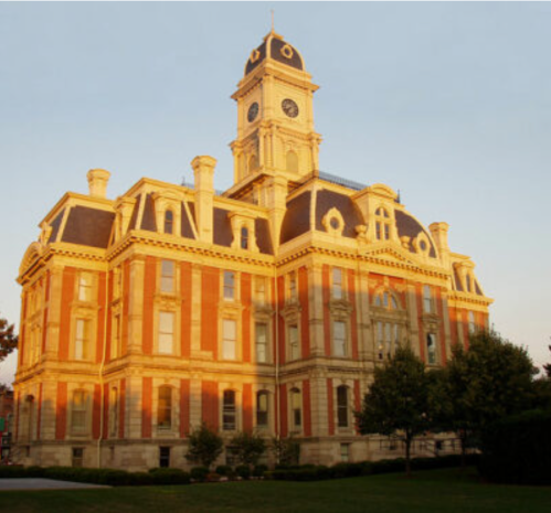Historic building with a clock tower, featuring ornate architecture and warm sunset lighting. Green trees in the foreground.
