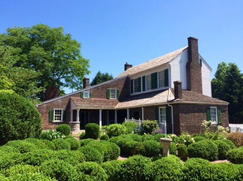A charming brick house with green shutters, surrounded by neatly trimmed bushes and a clear blue sky.