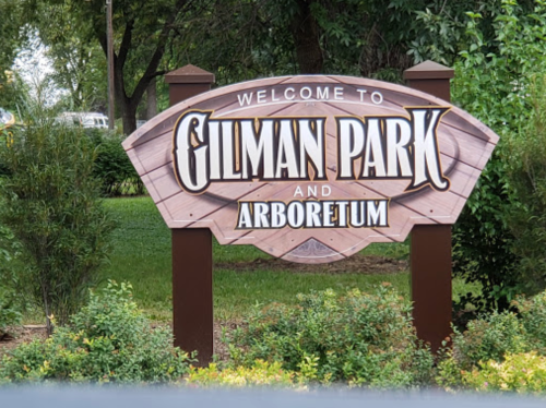 Sign welcoming visitors to Gilman Park and Arboretum, surrounded by greenery.