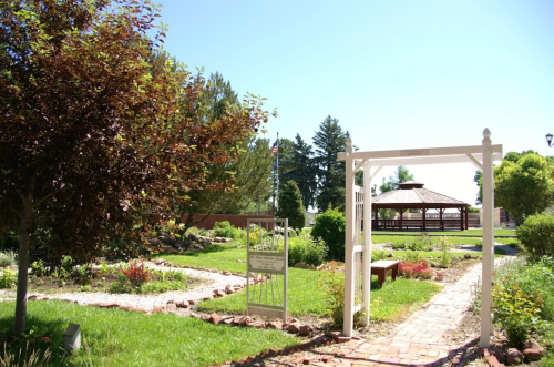 A garden path leads to a gazebo, framed by trees and colorful plants under a clear blue sky.