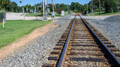 A view of railroad tracks extending into the distance, with grass and gravel alongside, and traffic signals in the background.