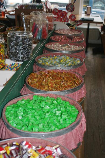 A colorful display of various candies in jars and baskets on a wooden table, creating a vibrant candy shop atmosphere.