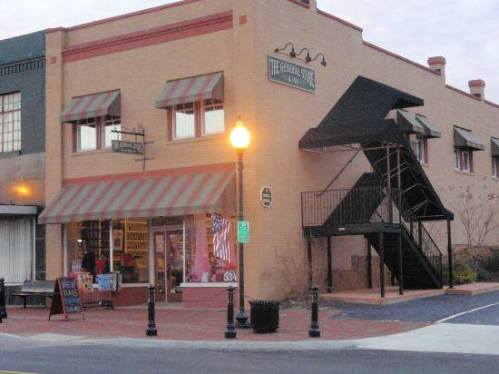 A brick building with striped awnings, a staircase, and a shop window displaying various items. Streetlights illuminate the scene.
