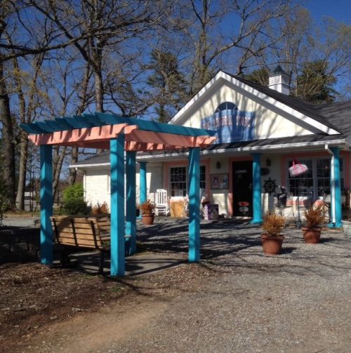 A charming building with a blue and pink awning, surrounded by trees and potted plants, inviting entrance.