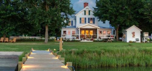 A charming house with a porch, surrounded by trees, viewed from a wooden dock leading to a grassy area.