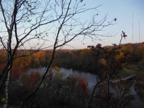 A serene view of a river surrounded by autumn foliage and bare trees, with radio towers in the distance.