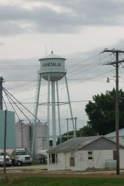 Water tower labeled "VANDALIA" with silos and a small house nearby, under a cloudy sky.