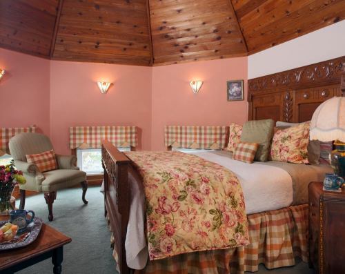 Cozy bedroom with a floral bedspread, wooden ceiling, and plaid accents, featuring a chair and a small table with snacks.