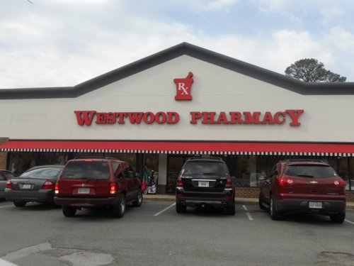 Exterior of Westwood Pharmacy building with a red and white sign, featuring parked cars in front.