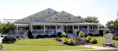 A large, charming building with a porch, decorated with patriotic bunting and surrounded by greenery.