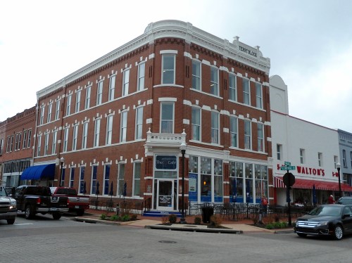 Historic brick building with large windows, featuring a café on the ground floor, located at a street corner.