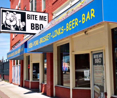 Exterior of "Bite Me BBQ" restaurant featuring a colorful awning and a sign with a cartoon pig.