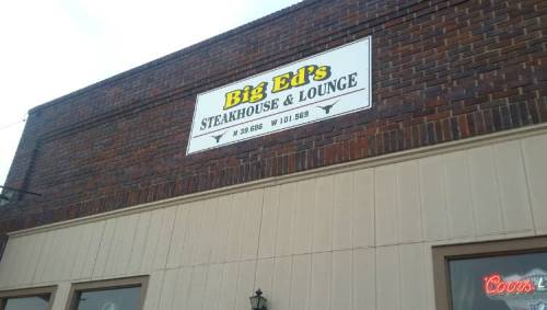 Sign for Big Ed's Steakhouse & Lounge on a brick building, featuring the restaurant's name and location coordinates.
