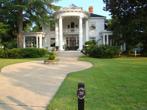A grand white house with columns, surrounded by greenery and a circular driveway, marked with the number 29.