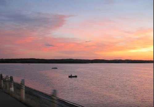 A serene sunset over a calm lake, with small boats silhouetted against the colorful sky.