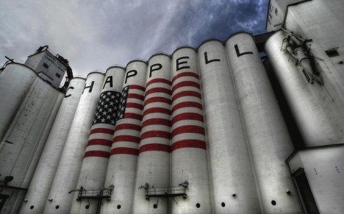 Silos with "CHAPPELL" painted on them, featuring a large American flag design on the front against a cloudy sky.