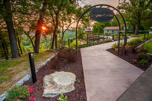 A scenic pathway leads to a Scripture Garden, framed by trees and a sunset in the background.