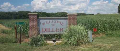 Sign welcoming visitors to Diller, surrounded by green fields and blue skies.