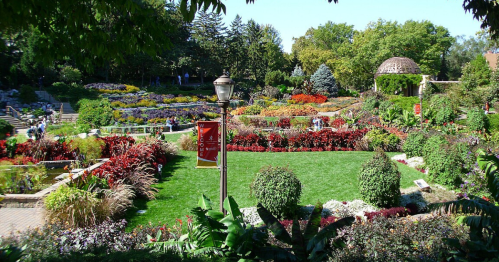 A vibrant garden filled with colorful flowers, greenery, and pathways, with people enjoying the scenery.